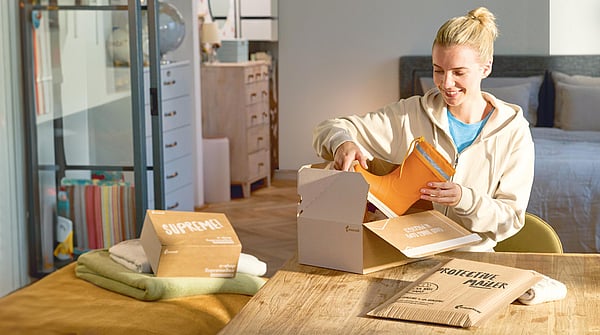 Woman sitting next to a table filled with Mondi packaging while unpacking a pair of rain boots.